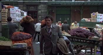 Movie still from “Frenzy” (1972), directed by Alfred Hitchcock – A man wearing a suit and tie walking down a street; Wide shot, Over the shoulder angle