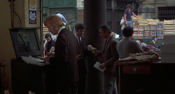 Movie still from “Frenzy” (1972), directed by Alfred Hitchcock – A group of people standing around a building eating food; Medium shot, Over the shoulder angle
