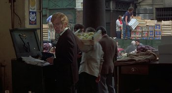 Movie still from “Frenzy” (1972), directed by Alfred Hitchcock – A group of people standing around a table; Medium shot, Over the shoulder angle