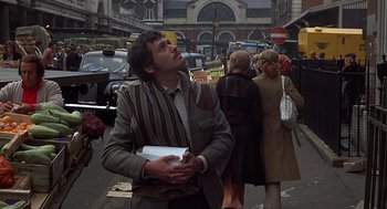 Movie still from “Frenzy” (1972), directed by Alfred Hitchcock – A man standing on the side of the street holding a book; Medium shot, Low angle