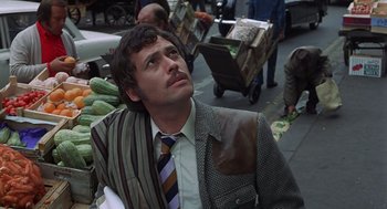Movie still from “Frenzy” (1972), directed by Alfred Hitchcock – A man wearing a suit and tie sitting in a market; Medium shot, Low angle