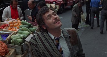 Movie still from “Frenzy” (1972), directed by Alfred Hitchcock – A man in a suit and tie sitting in front of a bunch of fruit; Medium shot, Low angle