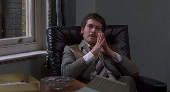 Movie still from “Frenzy” (1972), directed by Alfred Hitchcock – A man sitting in a chair with his hands clasped together; Medium shot, High angle