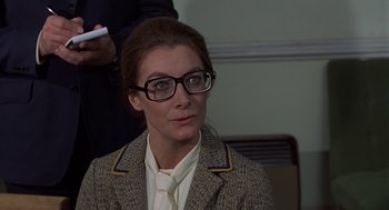Movie still from “Frenzy” (1972), directed by Alfred Hitchcock – A woman wearing glasses and a jacket is holding a wii controller; Close Up shot, Over the shoulder angle