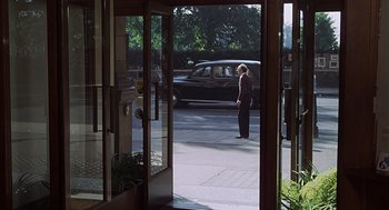 Movie still from “Frenzy” (1972), directed by Alfred Hitchcock – A woman standing in front of an open glass door; Wide shot, Over the shoulder angle