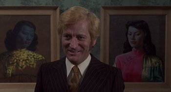 Movie still from “Frenzy” (1972), directed by Alfred Hitchcock – A man wearing a suit and tie standing in front of a picture; Close Up shot, Low angle
