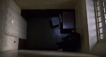 Movie still from “Frenzy” (1972), directed by Alfred Hitchcock – A person sitting in a dark room next to a chair; Wide shot, Overhead angle