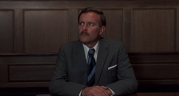 Movie still from “Frenzy” (1972), directed by Alfred Hitchcock – A man in a suit and tie sitting at a table with his arms crossed; Close Up shot, Low angle