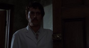 Movie still from “Frenzy” (1972), directed by Alfred Hitchcock – A man in a white lab coat standing in front of a door; Medium shot, Low angle