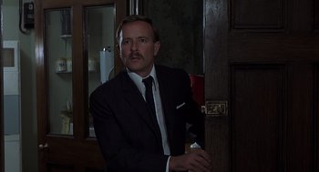 Movie still from “Frenzy” (1972), directed by Alfred Hitchcock – A man in a suit and tie standing in front of a door; Close Up shot, Low angle