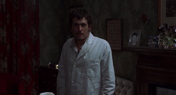 Movie still from “Frenzy” (1972), directed by Alfred Hitchcock – A man in a white lab coat standing in a dark room; Medium shot, Low angle