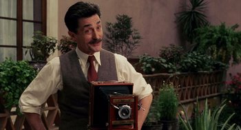 Movie still from “Frida” (2002), directed by Julie Taymor – A man in a vest and tie holding an old fashioned camera; Close Up shot, Low angle