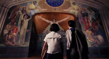 Movie still from “Frida” (2002), directed by Julie Taymor – Two people standing in front of a mural of an angel; Wide shot, Low angle