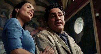 Movie still from “Frida” (2002), directed by Julie Taymor – A man and a woman sitting next to each other in front of a painting; Medium shot, Low angle