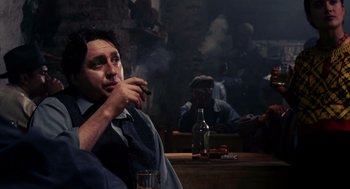 Movie still from “Frida” (2002), directed by Julie Taymor – A man sitting at a table smoking a cigarette; Medium shot, Over the shoulder angle