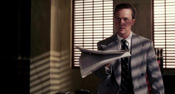 Movie still from “Frida” (2002), directed by Julie Taymor – A man in a suit and tie holding a newspaper; Medium shot, Over the shoulder angle