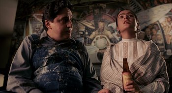 Movie still from “Frida” (2002), directed by Julie Taymor – A man and a woman sitting next to each other holding a beer; Medium shot, Low angle