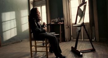 Movie still from “Frida” (2002), directed by Julie Taymor – A person sitting in a chair in front of an easel; Wide shot, High angle