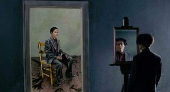 Movie still from “Frida” (2002), directed by Julie Taymor – A woman sitting on a chair in front of a mirror in a room; Medium shot, Over the shoulder angle