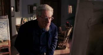 Movie still from “Frida” (2002), directed by Julie Taymor – An older man in a suit and tie looking at a picture; Medium shot, Over the shoulder angle