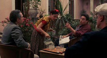 Movie still from “Frida” (2002), directed by Julie Taymor – A woman pouring a drink into a glass while a man watches; Medium shot, Over the shoulder angle