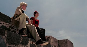 Movie still from “Frida” (2002), directed by Julie Taymor – An older man and woman sitting on top of a stone wall; Wide shot, Low angle