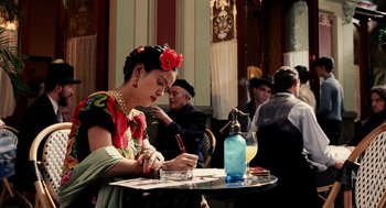 Movie still from “Frida” (2002), directed by Julie Taymor – A woman sitting at a table writing on a piece of paper; Medium shot, Over the shoulder angle