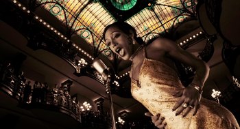 Movie still from “Frida” (2002), directed by Julie Taymor – A woman singing into a microphone in front of a stained - glass window; Medium shot, Low angle