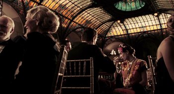 Movie still from “Frida” (2002), directed by Julie Taymor – A group of people sitting in a room with stained glass windows; Wide shot, Low angle