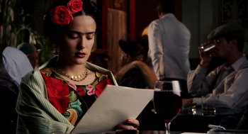 Movie still from “Frida” (2002), directed by Julie Taymor – A woman in a floral dress reading a paper; Close Up shot, Over the shoulder angle