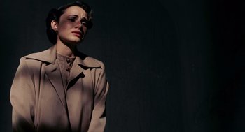 Movie still from “Frida” (2002), directed by Julie Taymor – A woman wearing a tan coat standing next to a wall; Close Up shot, High angle