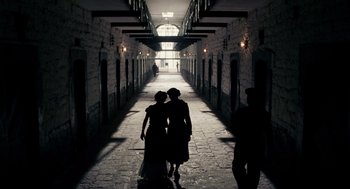 Movie still from “Frida” (2002), directed by Julie Taymor – Two women are walking down a hallway in a building; Wide shot, Over the shoulder angle