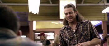 Movie still from “Friday Night Lights” (2004), directed by Peter Berg – A man with long hair is smiling for the camera; Medium shot, Over the shoulder angle