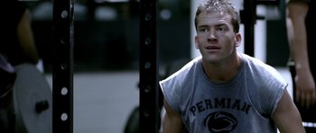 Movie still from “Friday Night Lights” (2004), directed by Peter Berg – A man in a gray t - shirt is in a gym; Close Up shot, Over the shoulder angle