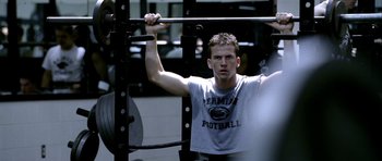 Movie still from “Friday Night Lights” (2004), directed by Peter Berg – A young man is lifting a barbell in a gym; Medium shot, Over the shoulder angle