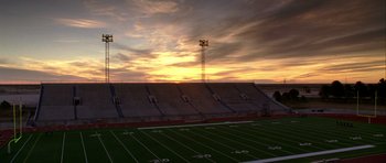 Movie still from “Friday Night Lights” (2004), directed by Peter Berg – An empty football field at sunset with the lights on; Extreme Wide shot, High angle