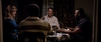 Movie still from “Friday Night Lights” (2004), directed by Peter Berg – A group of people sitting around a table with drinks; Medium shot, Over the shoulder angle