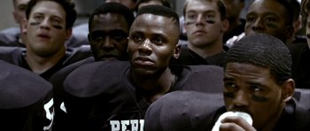 Movie still from “Friday Night Lights” (2004), directed by Peter Berg – A group of men sitting next to each other in a room; Close Up shot, Over the shoulder angle