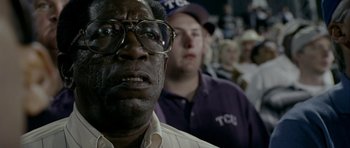 Movie still from “Friday Night Lights” (2004), directed by Peter Berg – A man with glasses is looking at a crowd; Close Up shot, Low angle