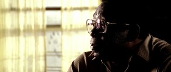 Movie still from “Friday Night Lights” (2004), directed by Peter Berg – An older man wearing glasses looking off into the distance; Extreme Close Up shot, Low angle