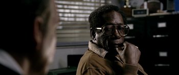 Movie still from “Friday Night Lights” (2004), directed by Peter Berg – An older man wearing glasses and a brown jacket; Close Up shot, Over the shoulder angle
