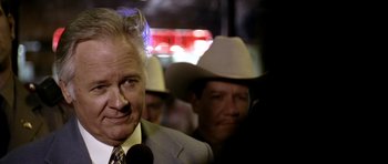 Movie still from “Friday Night Lights” (2004), directed by Peter Berg – A man in a suit and a cowboy hat is being interviewed; Close Up shot, Over the shoulder angle