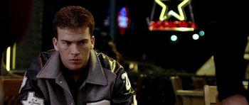 Movie still from “Friday Night Lights” (2004), directed by Peter Berg – A man in a leather jacket is sitting in front of a neon sign; Close Up shot, Over the shoulder angle