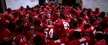 Movie still from “Friday Night Lights” (2004), directed by Peter Berg – A group of football players huddle together in a huddle; Wide shot, High angle