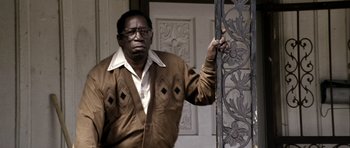 Movie still from “Friday Night Lights” (2004), directed by Peter Berg – An older man standing in front of an iron gate; Medium shot, Low angle