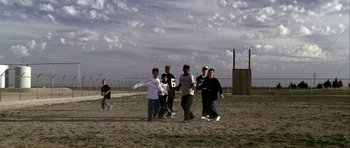 Movie still from “Friday Night Lights” (2004), directed by Peter Berg – A group of young men standing on top of a dirt field; Extreme Wide shot, High angle