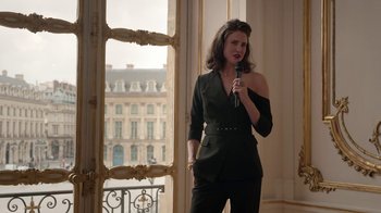 Movie still from “Emily in Paris” (2020), created by Darren Star – A woman in a black outfit is holding a microphone; Medium shot, Low angle