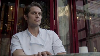 Movie still from “Emily in Paris” (2020), created by Darren Star – A man in a chef's outfit sitting in front of a window; Close Up shot, Low angle
