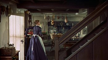 Movie still from “Friendly Persuasion” (1956), directed by William Wyler – A woman standing in front of an open fire place; Wide shot, High angle