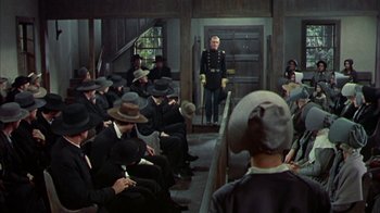Movie still from “Friendly Persuasion” (1956), directed by William Wyler – A group of people sitting in a room with hats on; Wide shot, High angle